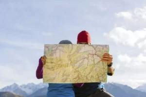 A husband and wife, with their faces hidden behind a large map, study their route in the mountains, embodying a “think outside the box” approach to exploration and discovery, especially when it comes to their date nights together.