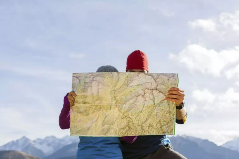 A husband and wife, with their faces hidden behind a large map, study their route in the mountains, embodying a “think outside the box” approach to exploration and discovery, especially when it comes to their date nights together.