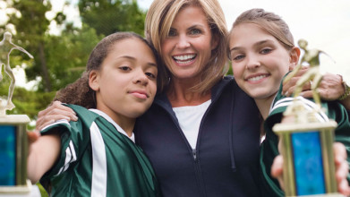 Proud, happy mom hugging two teen soccer champion girls who are holding out their tropies toward the camera