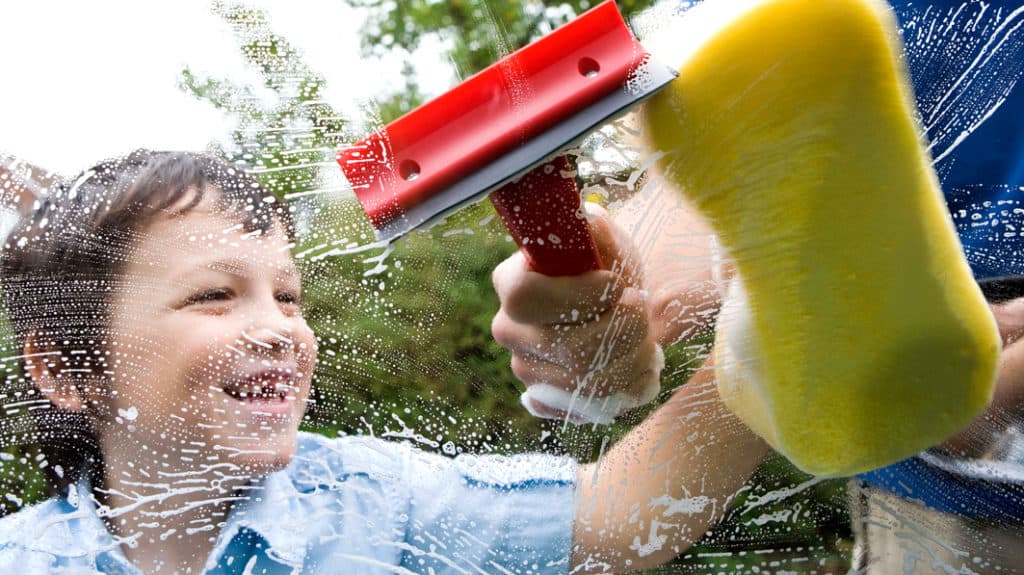 Young boy and his dad washing a window with a sponge and squeegee