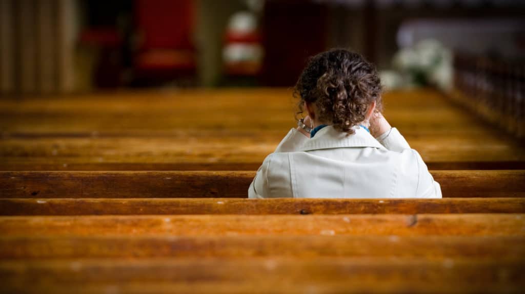 a woman sits silently in church considering weather or not to go to an abortion clinic.
