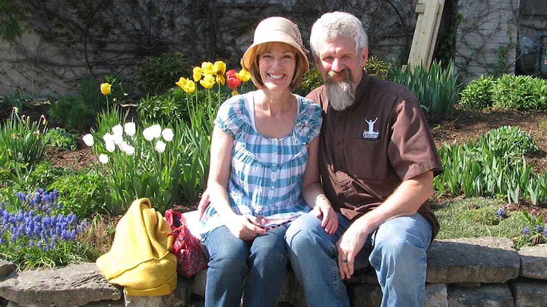 Mac and Mary Owen sitting together on a ledge in front of a flower garden