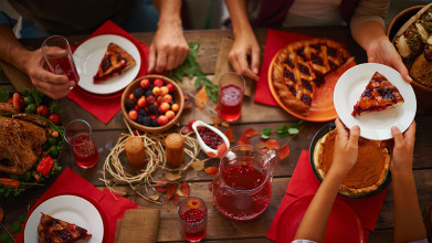 Hands on a table with a red tablecloth and a Thanksgiving meal.