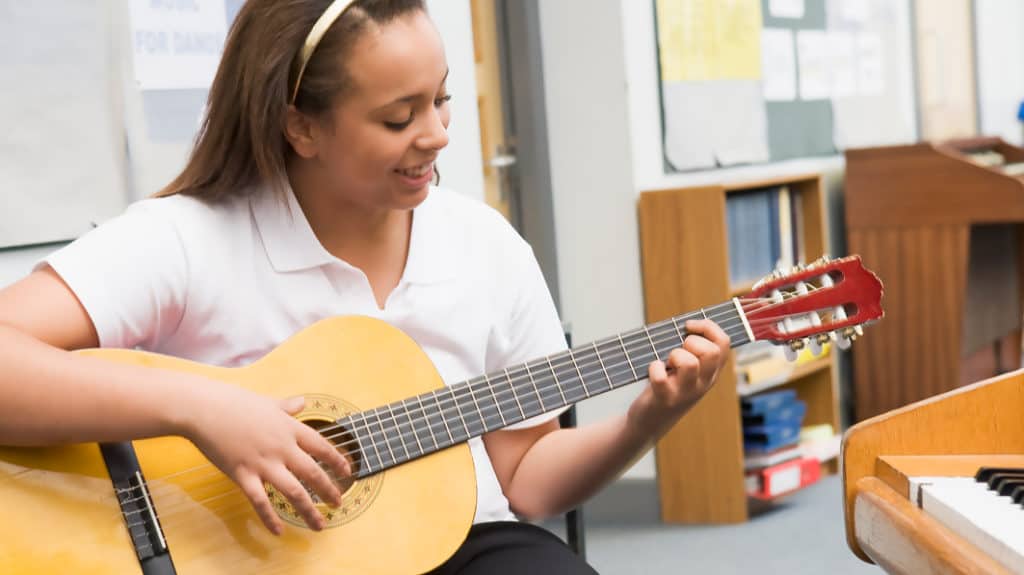Teen girl learning guitar in classroom