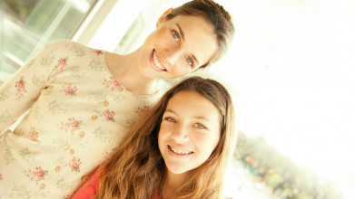 Smiling mom and teen daughter standing together, posing for the camera