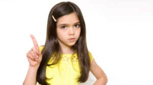 Serious-looking young girl in yellow dress pointing her finger in the air, like she’s wagging it in disapproval
