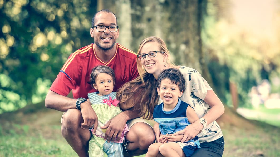 Smiling mom and dad crouching down with their two young adopted kids, posing for a picture in the park