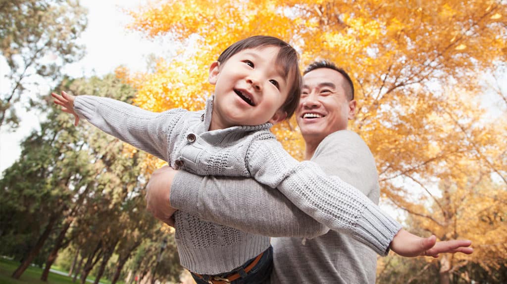 Joyful dad swinging his young, smiling son in a park on an autumn day