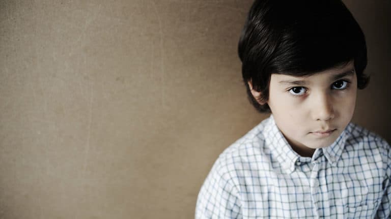 A lone, serious-looking boy with dark hair, looking into the camera