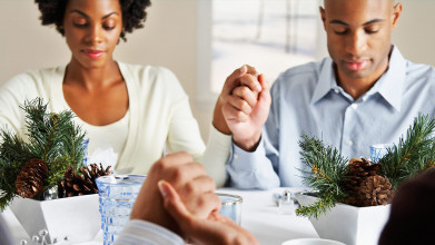 Family saying grace around the dinner table, with focus on one couple holding hands