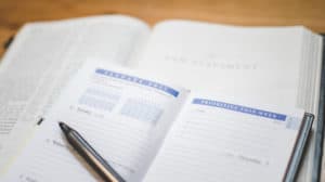 Close up of an appointment book and pen lying on top of an open bible