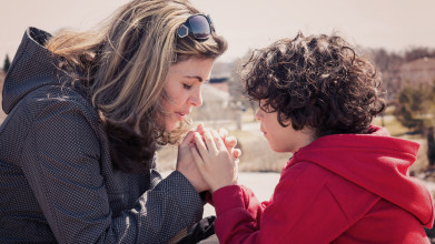 Mom and young son holding hands as they pray together outside