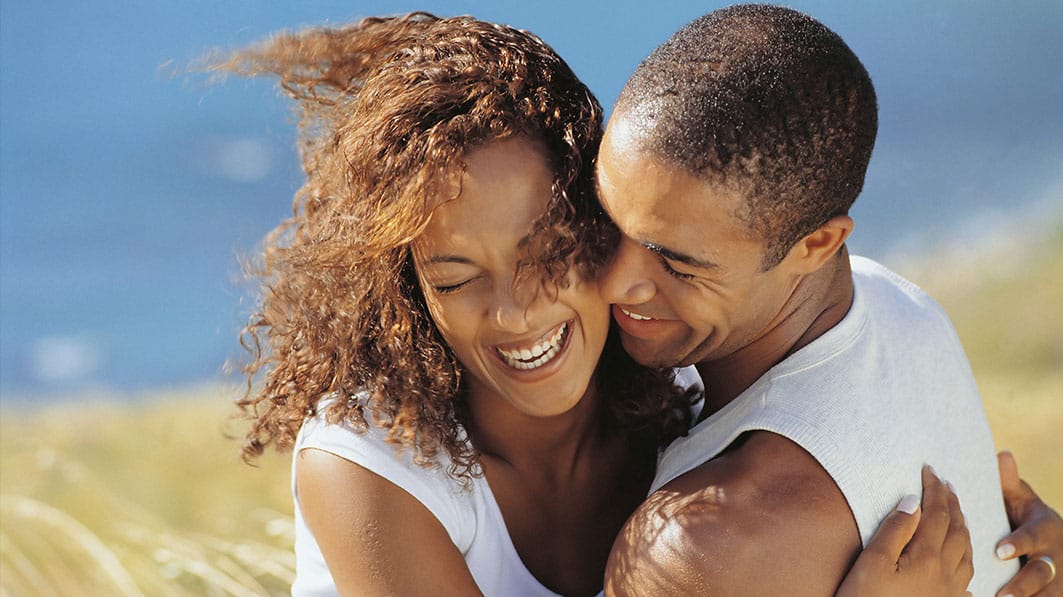Close-up of African-American couple laughing and hugging outside. 