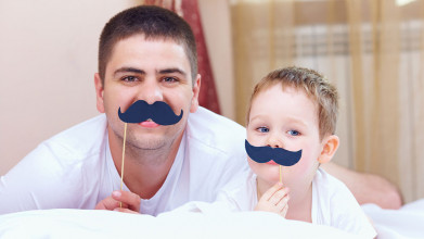 Father and young son playfully holding up paper mustaches on their face