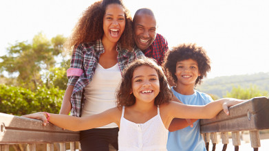 Laughing parents posing for photo with their two young, smiling children on a narrow walkway type of bridge