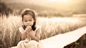 Sad child sitting alone on wall outdoors