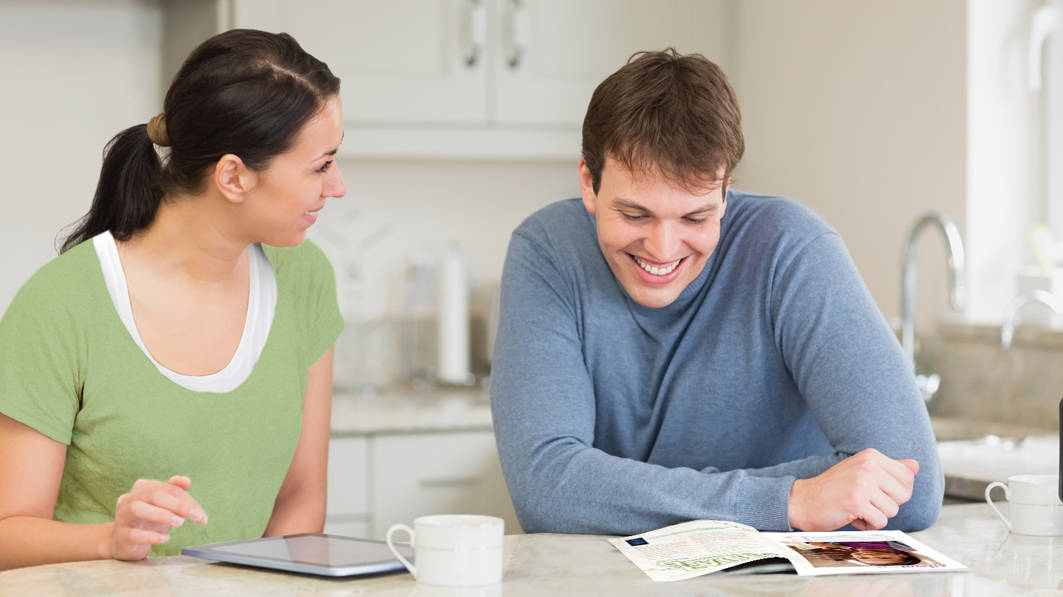 Married couple sitting in the kitchen having fun reading and talking