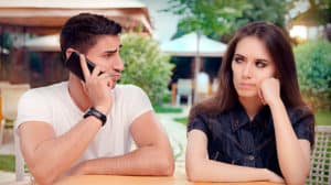 Young couple sitting outside looking unhappily at each other while he's on the phone