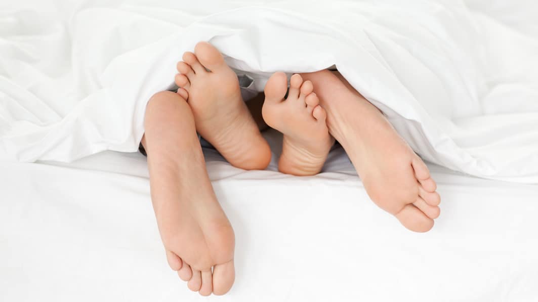 A couple's bare feet poking out from under the covers