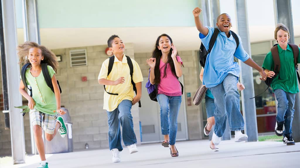 Group of school children excitedly running down a campus sidewalk