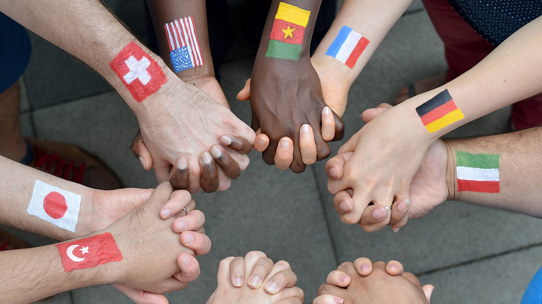 International brothers and sisters in a circle with flags of different countries painted on their wrists