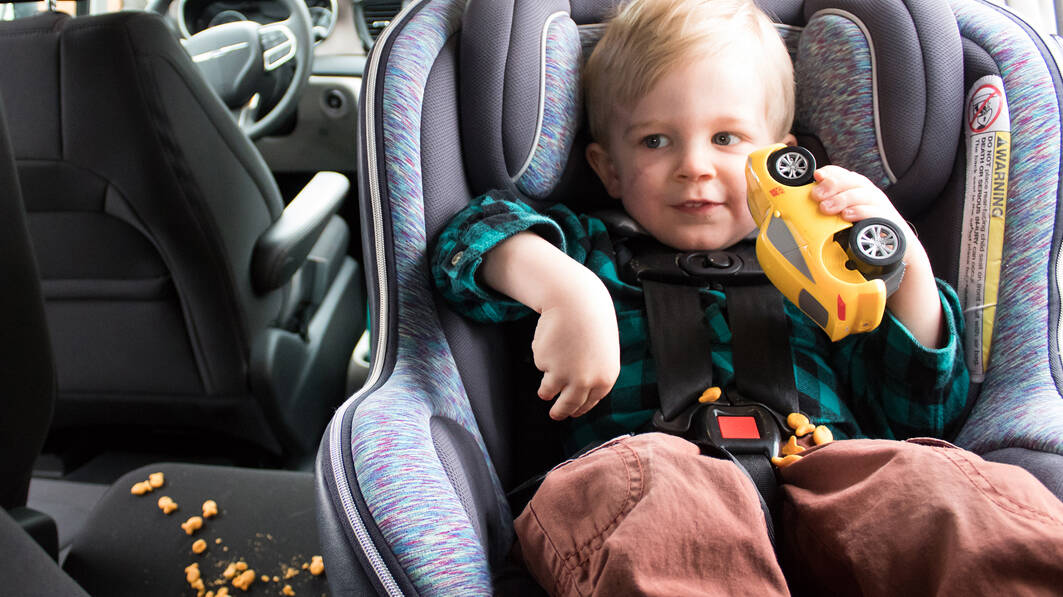 A toddler is buckled into his car seat and Goldfish crumbs are scattered around
