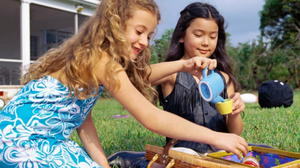 Two young girls outdoors pouring tea with a play set