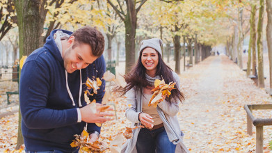 Couple laughing and playing as she throws fallen tree leaves at him on an Autumn day in the park