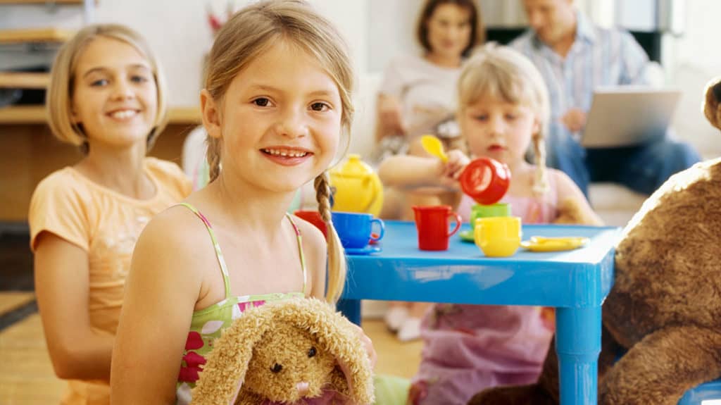 Young daughters have a play tea party while parents watch in background