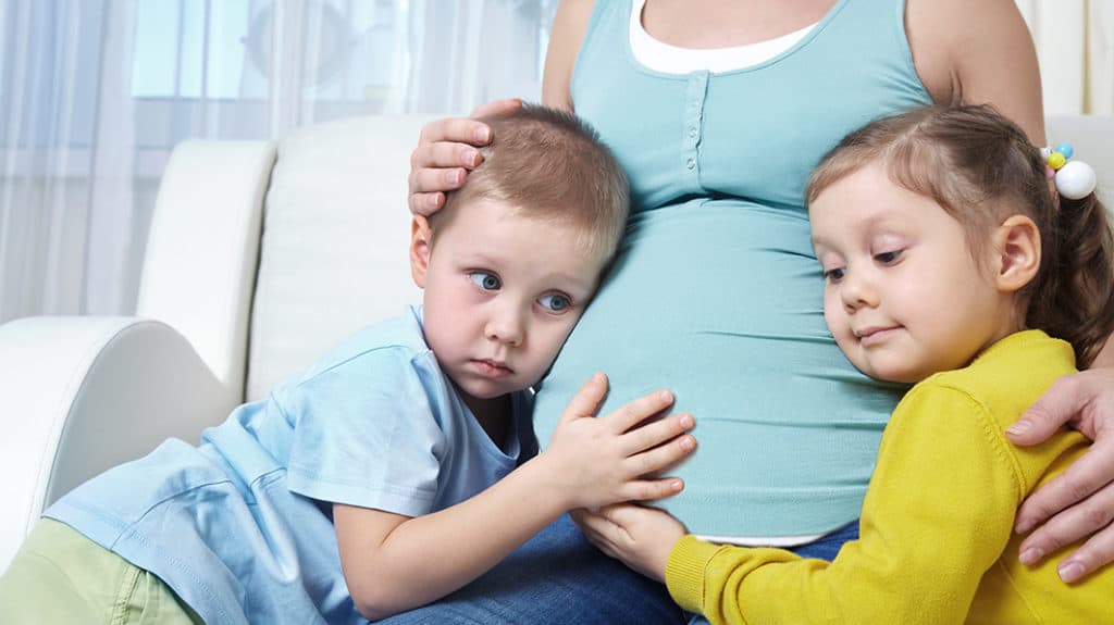 Pregnant mother with her two children who have their ears on the baby within