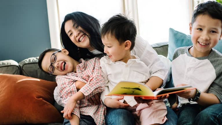 A mother and her three sons laugh together on the sofa