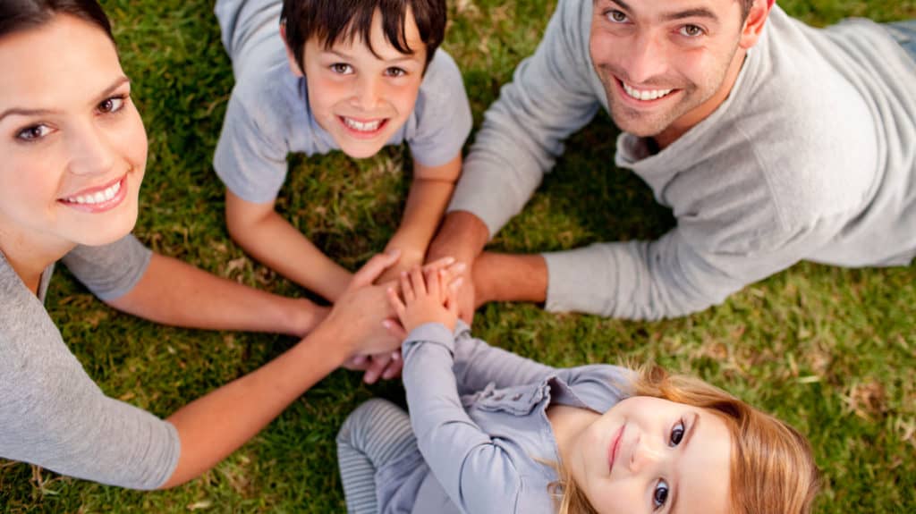 Mom, dad and two children stack their hands as a team as they create a parenting strategy