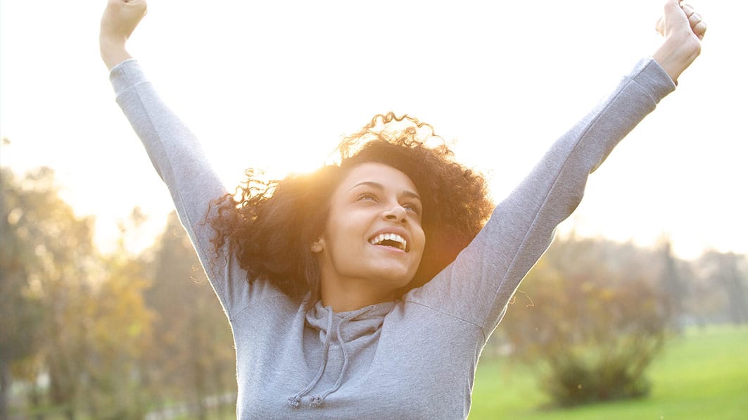 Joyful woman standing outside, raising her arms in the air as in victory