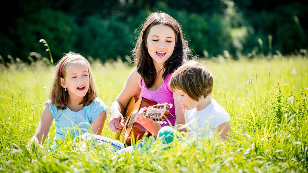 Mom playing guitar and singing with young daughters
