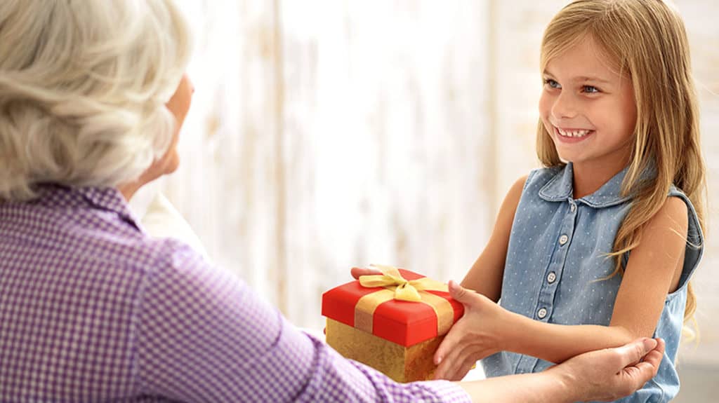 A granddaughter hands a wrapped package to her grandmother