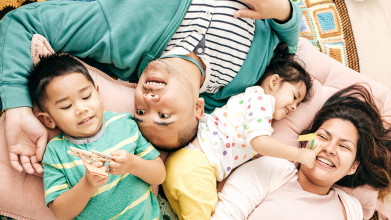 Shown from above, a joyful, playful family lying down; two young kids, a brother and sister, are playing with clothespins