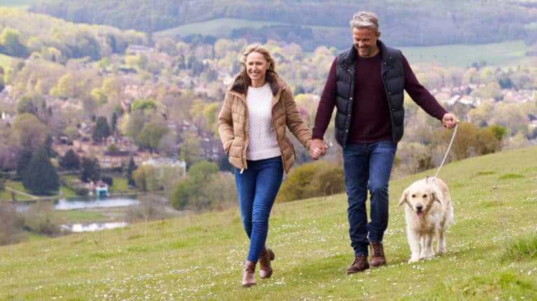 Couple taking golden retriever for a walk on hillside above town