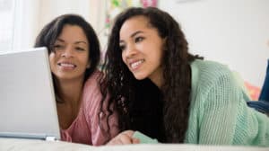 Mother and teen daughter using laptop on bed