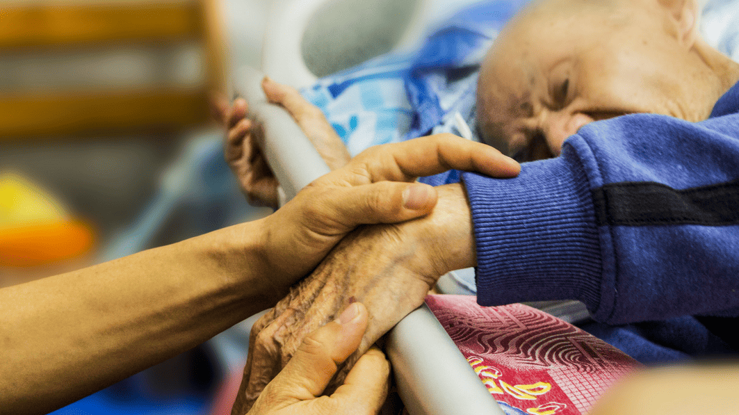 Hands hold the hand of a sick loved one in hospital bed