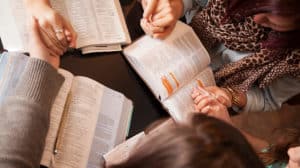 Shown from above, two couples holding hands and praying during a Bible study