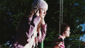 Two teen girls sit on swings and look longingly into the distance