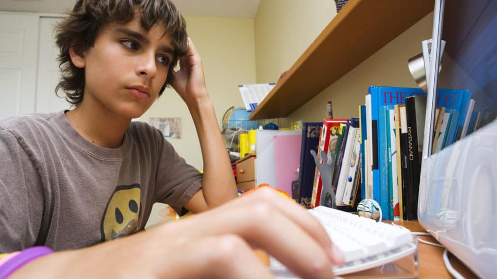 Serious-looking teen boy sitting at computer