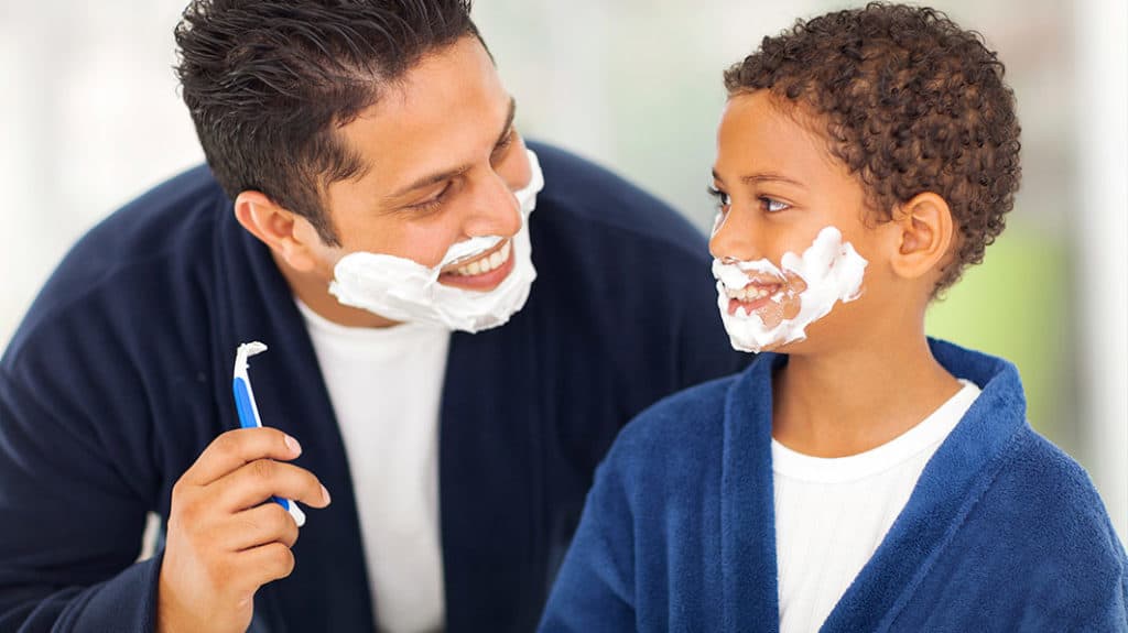 Dad teaching his son how to shave with a hand razor and shaving cream