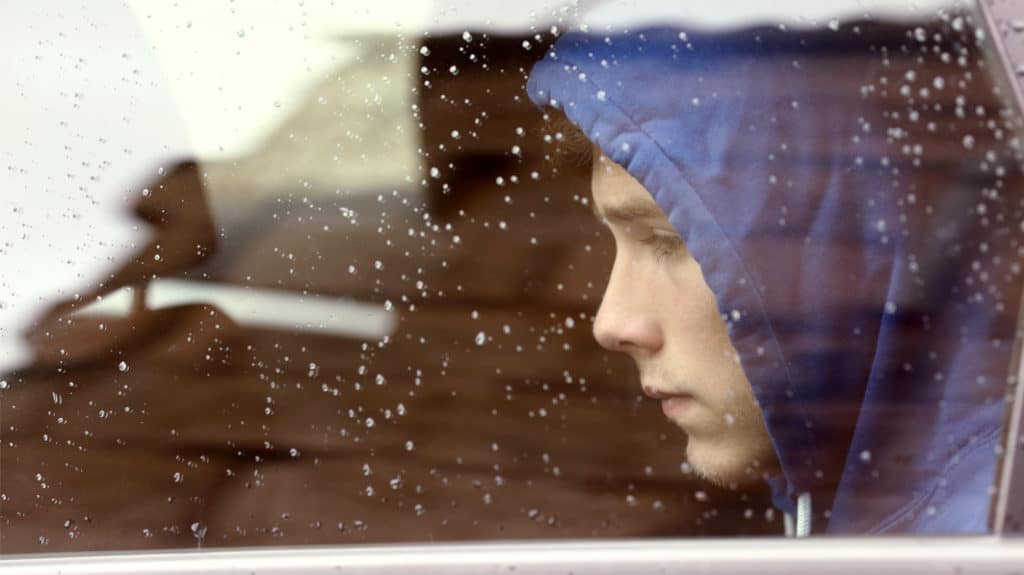 Pensive teen boy sitting in rain splattered car