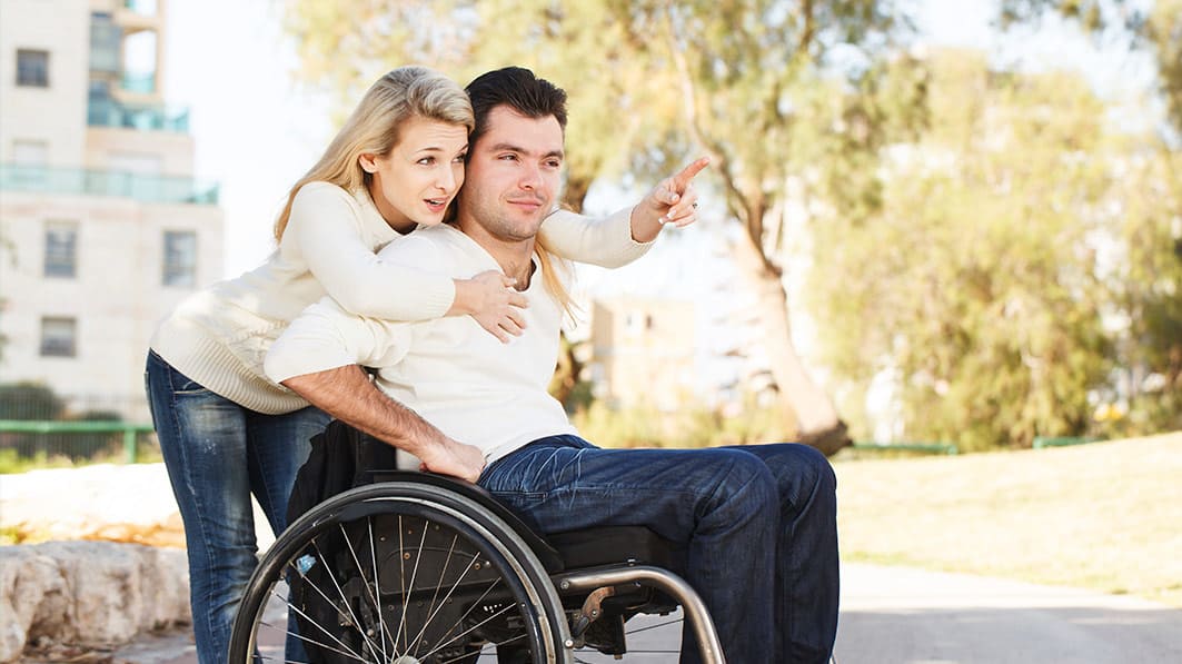Man in wheelchair hugged from behind by a standing woman who's pointing, showing him something