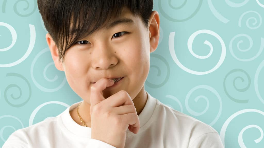 Tween-age boy looking at camera and thinking with his finger held to his lips