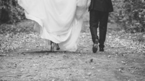 Newlyweds walking down outdoor path away from camera