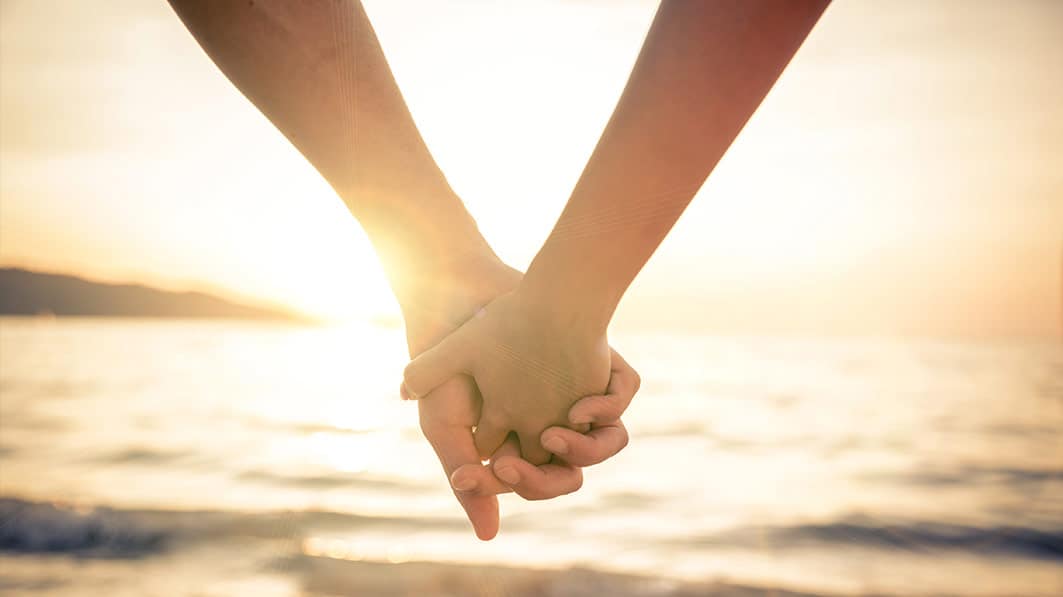 Close up of a couple's holding hands as they look out over a lake