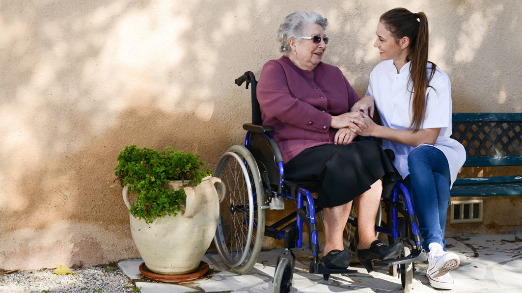 Smiling young woman talking with elderly woman in a wheelchair