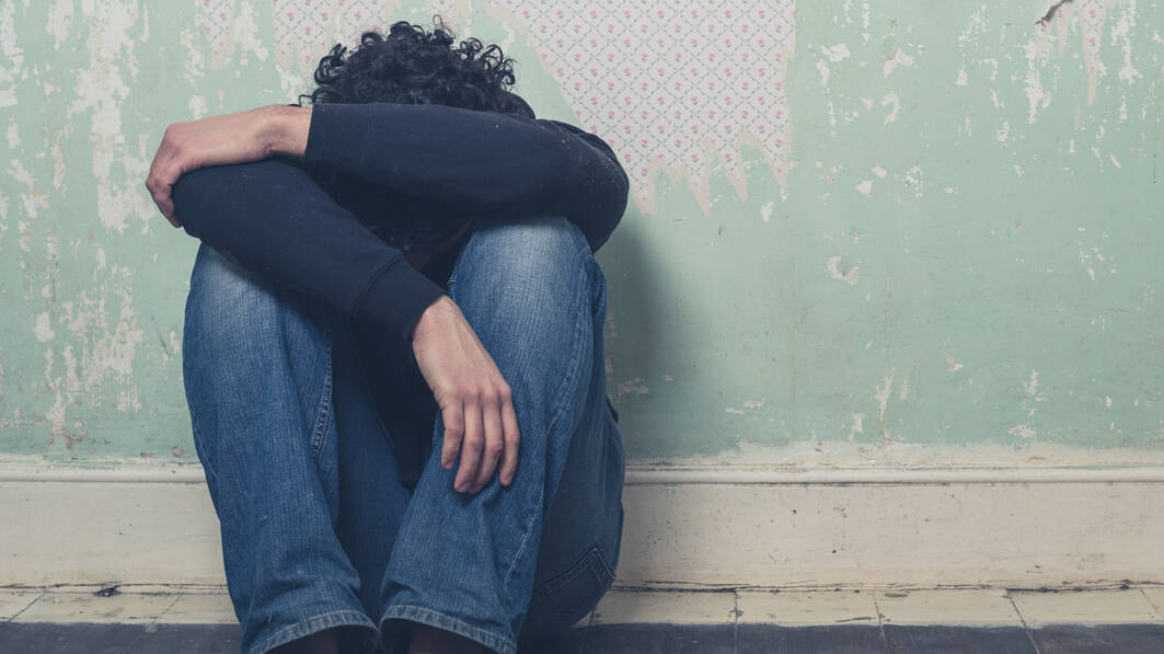 Sad young man sitting on a floor against a wall with his head down